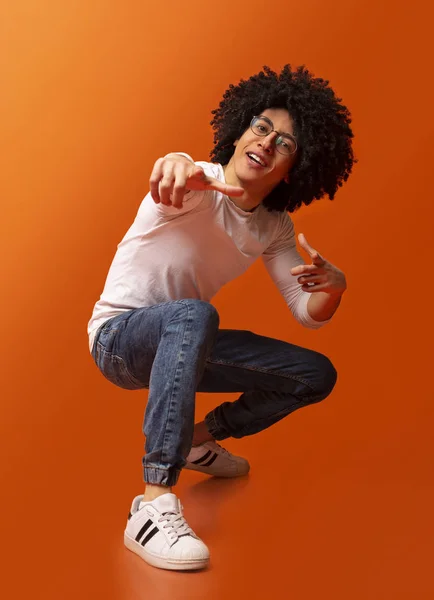 Cocky millennial chico apuntando a la cámara, en cuclillas sobre fondo naranja —  Fotos de Stock