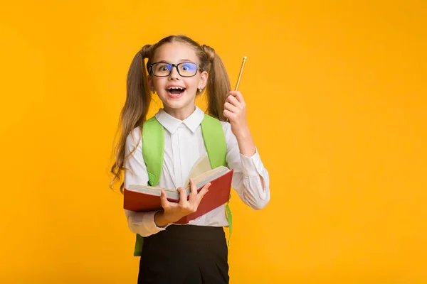 First-Grade Schoolgirl Segurando Livro e Lápis em fundo de estúdio amarelo — Fotografia de Stock