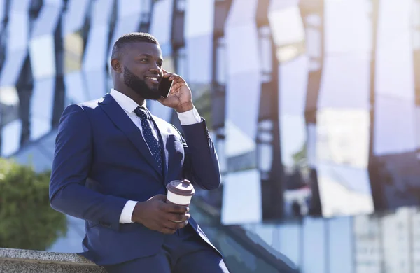 Hombre de negocios hablando por celular sosteniendo la taza de café sentado al aire libre — Foto de Stock