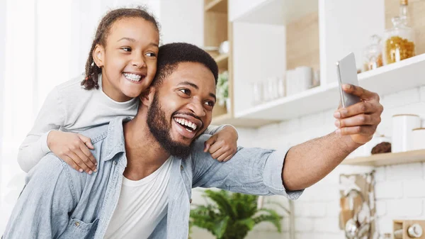 Afro papá y su hija tomando selfie en smartphone en la cocina —  Fotos de Stock