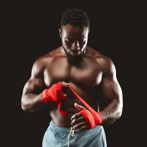 Strong african american man wrapping hands with boxing wraps