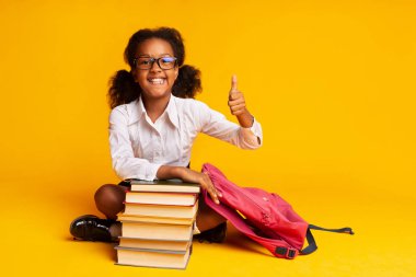 Afro Schoolgirl Gesturing Thumbs-Up Kitap Stack, Studio Shot at Oturan