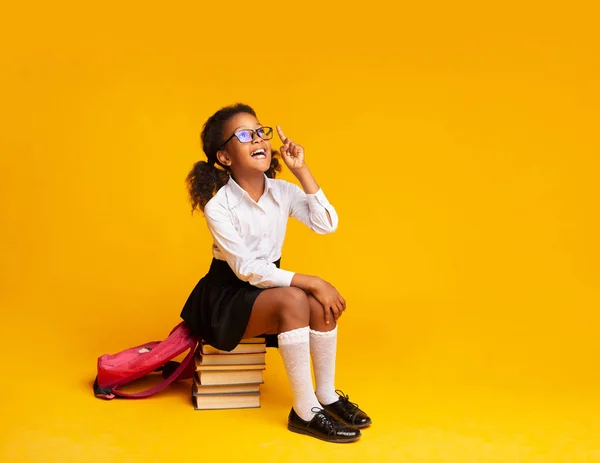 Carino afro studentessa puntando dito fino seduto su libro stack — Foto Stock