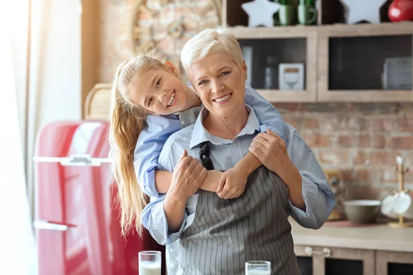 Внучка обнимает свою счастливую бабушку на домашней кухне — стоковое фото