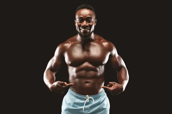 Lächelndes afrikanisches Fitnessmodel zeigt auf seine Sixpacks — Stockfoto