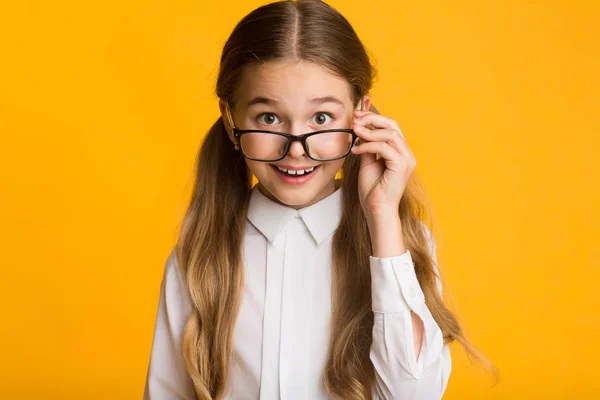 Schattig schoolmeisje kijkt uit over brillen op gele achtergrond — Stockfoto