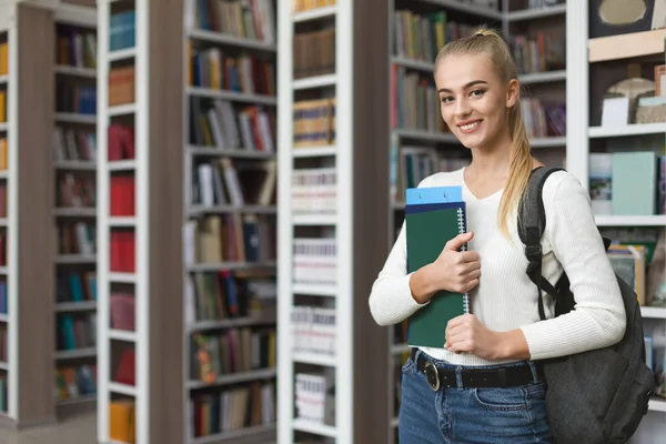 Menina loira bonita de pé ao lado de estantes na biblioteca — Fotografia de Stock