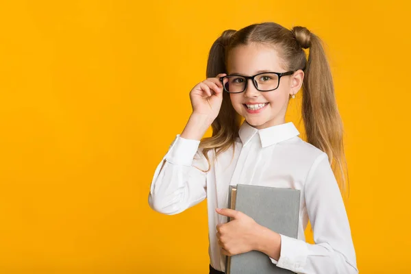 Sorrindo primeira classe escola menina segurando livro posando em fundo amarelo — Fotografia de Stock