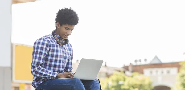 Adolescente africano alegre digitando no laptop conversando com amigos ao ar livre — Fotografia de Stock