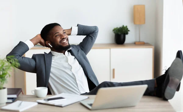 Munter afrikansk medarbejder lytter yndlingsmusik i øretelefoner på kontoret - Stock-foto