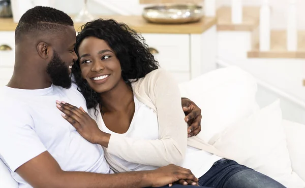 Young couple sitting on couch at home, cuddling each other — Stock Photo, Image