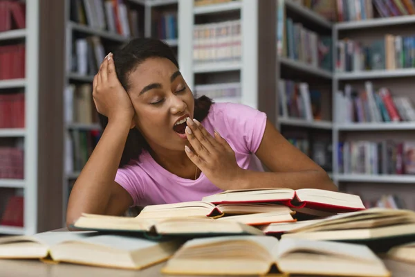 Chica afro cansada bostezando mientras lee libros en la biblioteca — Foto de Stock