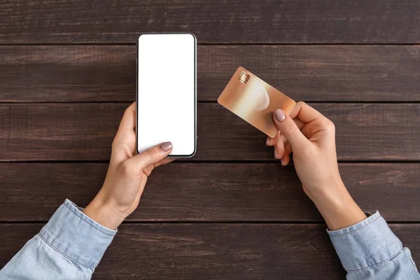 Жінка тримає кредитну картку і використовує мобільний телефон для фінансових операцій — стокове фото