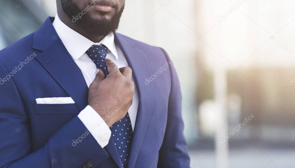 Bearded Afro Businessman Adjusting Tie In Urban Area, Cropped