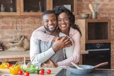 Grateful african woman hugging her husband at kitchen clipart