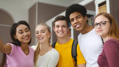 Happy multiracial young students taking selfie at library