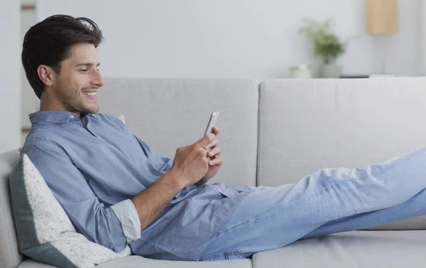 Homem feliz usando Smartphone Navegação Internet Deitado no sofá — Fotografia de Stock