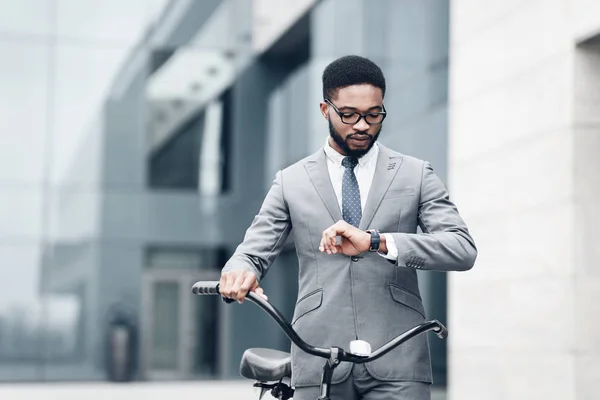 Afro empresário verificando o tempo, andando de escritório em bicicleta — Fotografia de Stock