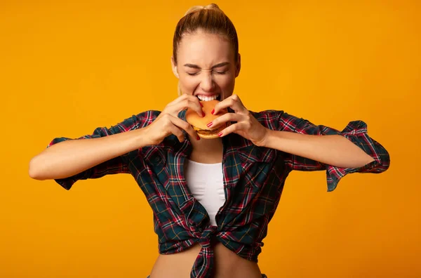 Σπορ κορίτσι δάγκωμα Burger σε κίτρινο φόντο — Φωτογραφία Αρχείου