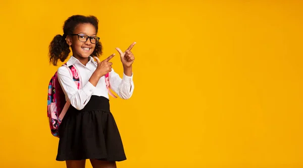 Alegre colegiala negra señalando los dedos en el espacio de copia, fondo amarillo — Foto de Stock