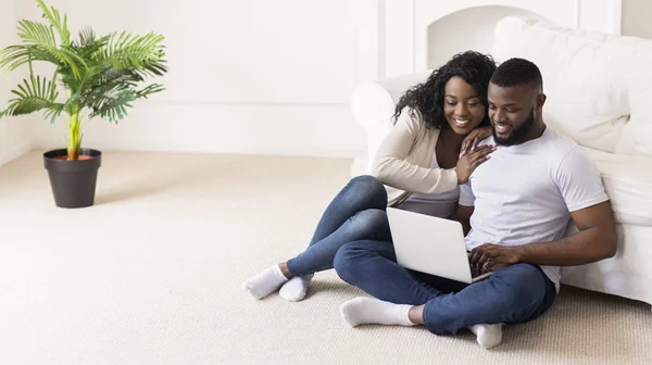 Schwarzes Paar kauft Möbel online sitzend auf dem Boden mit Laptop — Stockfoto