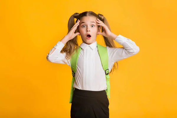 Geschokt elementaire student meisje clutching hoofd over gele achtergrond — Stockfoto