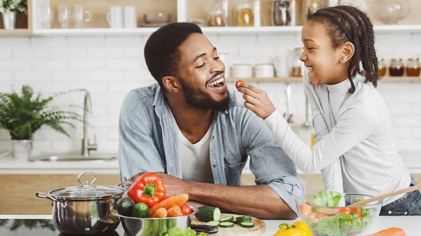 Mignonne africaine fille donnant son père cerise tomate tout en cuisinant — Photo