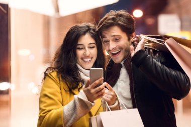 Kadın erkek akıllı telefon gösteren, açık havada alışveriş ten sonra yürüyüş