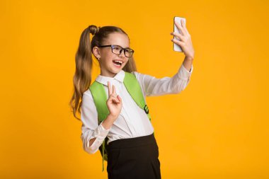 Schoolgirl Kullanarak Smartphone Selfie Gesturing V-Sign, Sarı Arka Plan alarak