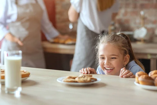 Чарівна маленька дівчинка на кухні дивиться з радістю на цукерки — стокове фото