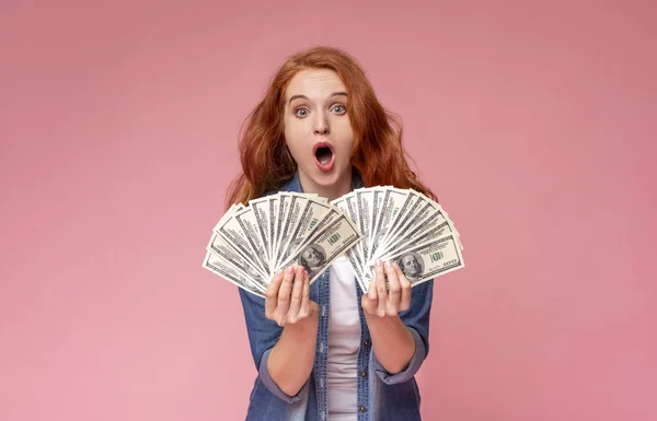 Шокированная рыжая девушка с кучей денег и криками — стоковое фото