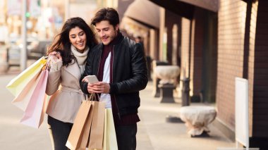 Birlikte alışveriş. Bin yıllık çift akıllı telefon açık havada kullanarak