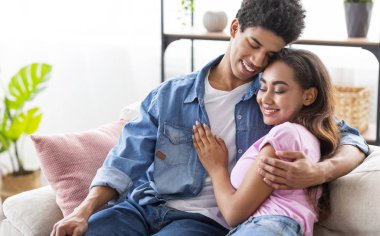 Evde kanepede oturan, birbirlerine sarılan gençler