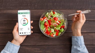 Kadın sebze salatası yiyor ve mobil uygulamada kalori sayma