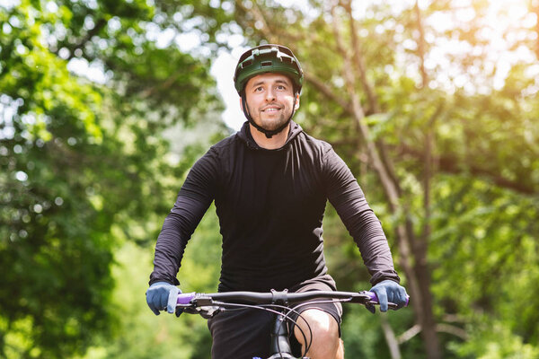 Portrait of cheerful young biker riding bicycle in greens