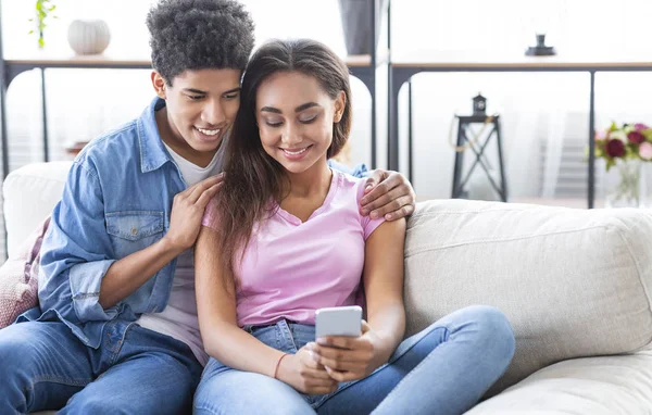 Millennial pareja negra navegando por las redes sociales en el teléfono inteligente en casa — Foto de Stock