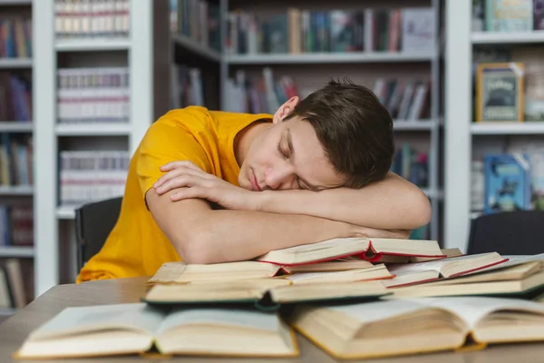 Trött ung kille tupplur på böcker i biblioteket — Stockfoto