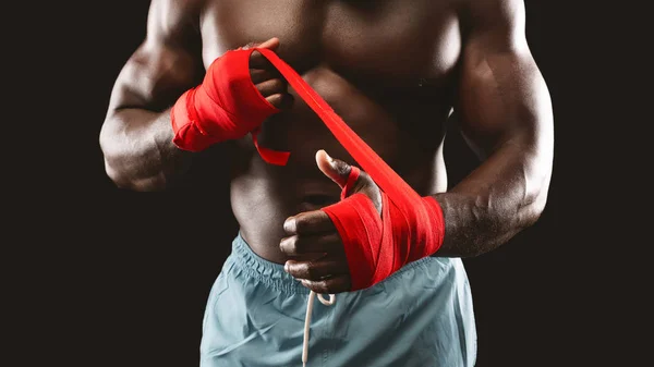 Professional black kickboxer rolling red wraps over wrists