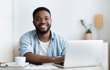 Afrikalı işçi dizüstü bilgisayar kullanarak, gülümseyen ve ofiste kahve içme