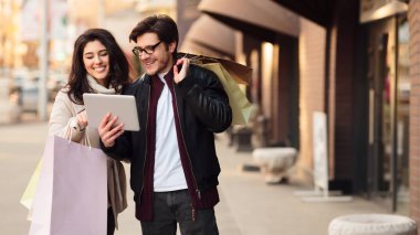 Şehir merkezinde alışveriş yaptıktan sonra tablet kullanan mutlu çift