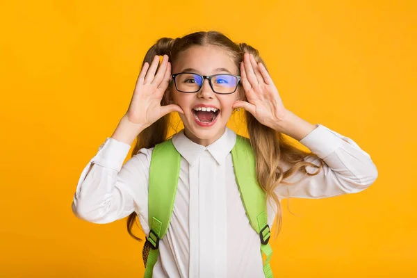 Ragazza elementare studente gridando tenendo le mani vicino alla bocca, sfondo giallo — Foto Stock