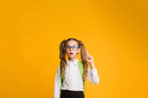 Scuola elementare ragazza puntando dito su sfondo giallo — Foto Stock