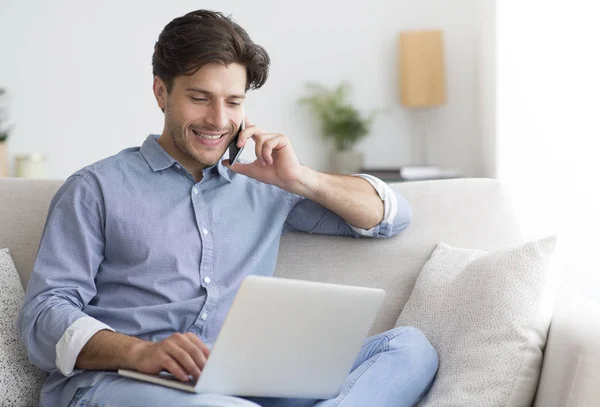 Jovem empreendedor conversando no celular trabalhando no laptop em casa — Fotografia de Stock