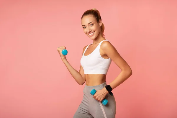 Mujer alegre haciendo ejercicio con sombrillas sobre fondo rosa — Foto de Stock