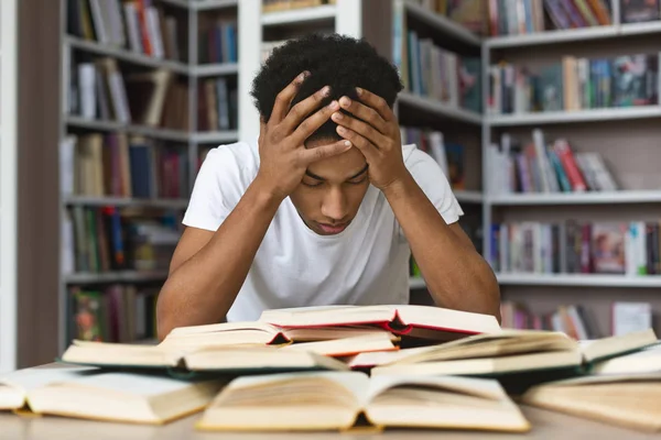 Exausto cara negro segurando a cabeça e lendo livro na biblioteca — Fotografia de Stock