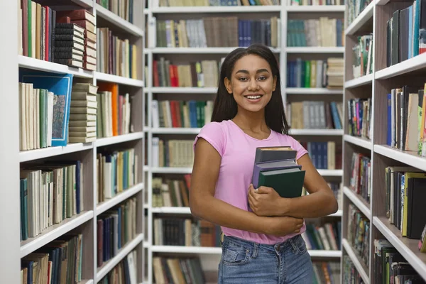 Vidám fekete lány áll között könyvespolcok könyvtár — Stock Fotó