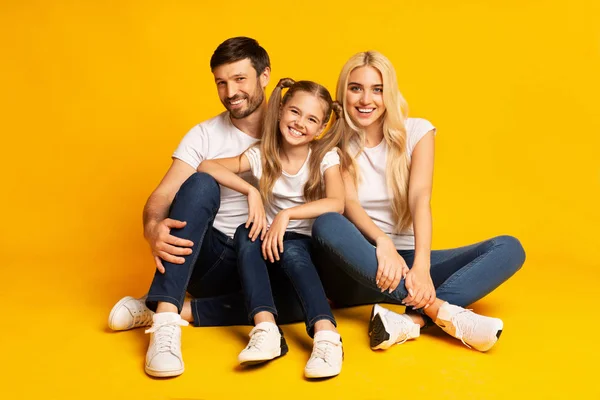 Eltern und Tochter umarmen sich sitzend auf gelbem Hintergrund — Stockfoto