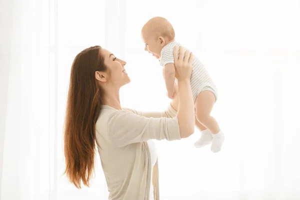 Sorrindo mãe levantando seu bebê recém-nascido adorável no ar — Fotografia de Stock