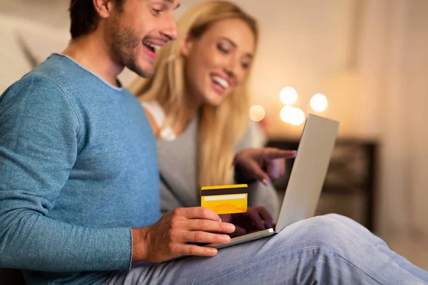 Cônjuges usando laptop e cartão de crédito sentado no sofá interior — Fotografia de Stock