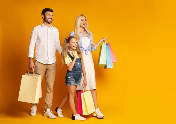 Padres e hija caminando sosteniendo bolsas de compras, fondo amarillo —  Fotos de Stock